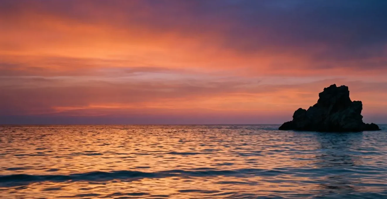 Vasto gradient cromatico di un tramonto mediterraneo con silhouette dell'isolotto di Es Vedrà all'orizzonte, palette arancio-rosa-blu intensi e riflessi dorati sull'acqua